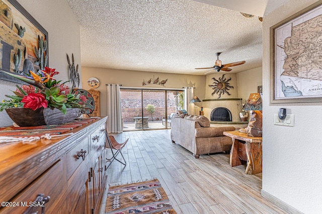 living room with a textured ceiling, light wood-type flooring, and ceiling fan