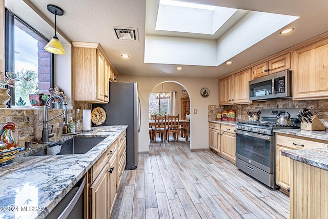 kitchen featuring a skylight, light stone countertops, sink, and appliances with stainless steel finishes