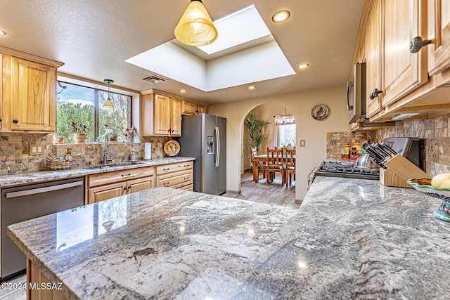 kitchen with light stone countertops, sink, backsplash, pendant lighting, and appliances with stainless steel finishes