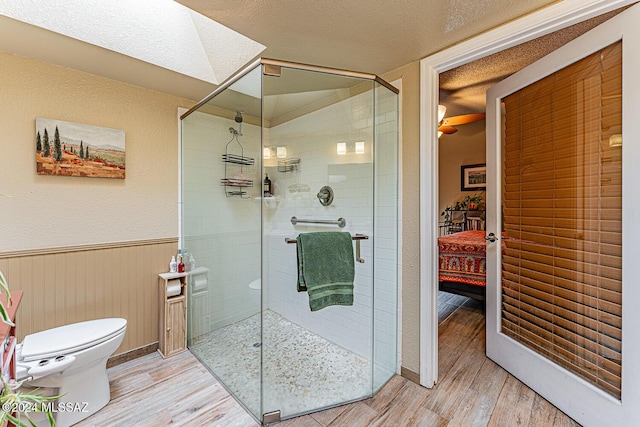 bathroom featuring a skylight, an enclosed shower, toilet, wooden walls, and hardwood / wood-style flooring