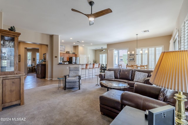 carpeted living room with ceiling fan with notable chandelier