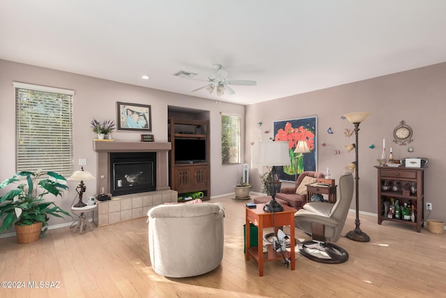 living room featuring a tiled fireplace, ceiling fan, plenty of natural light, and light wood-type flooring