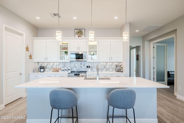 kitchen with white cabinetry, sink, decorative light fixtures, a kitchen island with sink, and appliances with stainless steel finishes