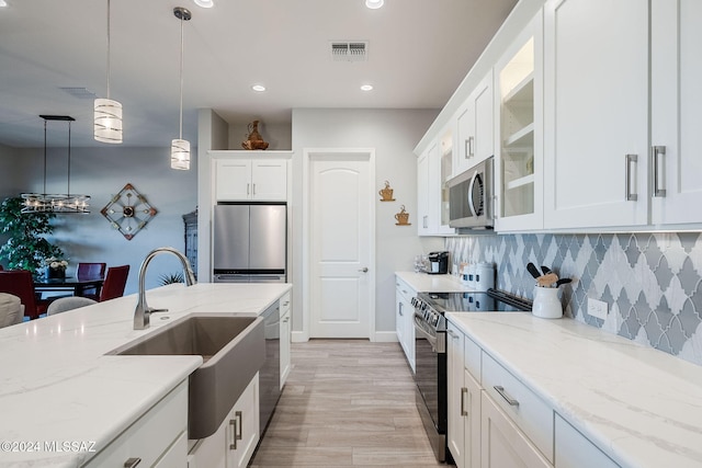 kitchen featuring white cabinets, appliances with stainless steel finishes, light stone countertops, and pendant lighting