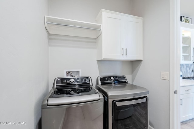 clothes washing area with cabinets and washing machine and dryer