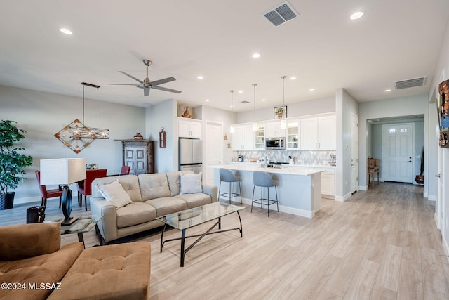 living room with ceiling fan, sink, and light wood-type flooring