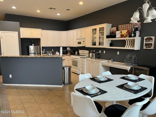 kitchen with white appliances, an inviting chandelier, white cabinets, light tile patterned floors, and an island with sink