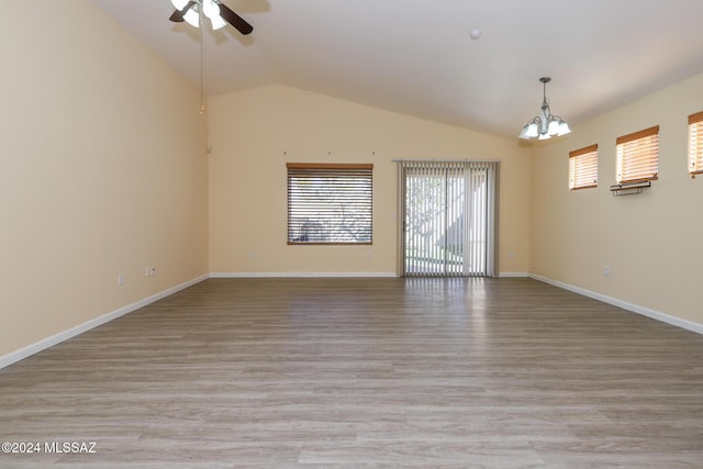 empty room featuring ceiling fan with notable chandelier, light wood-type flooring, and vaulted ceiling