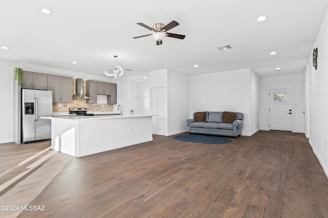 kitchen featuring decorative backsplash, wall chimney exhaust hood, stainless steel appliances, a center island with sink, and dark hardwood / wood-style floors