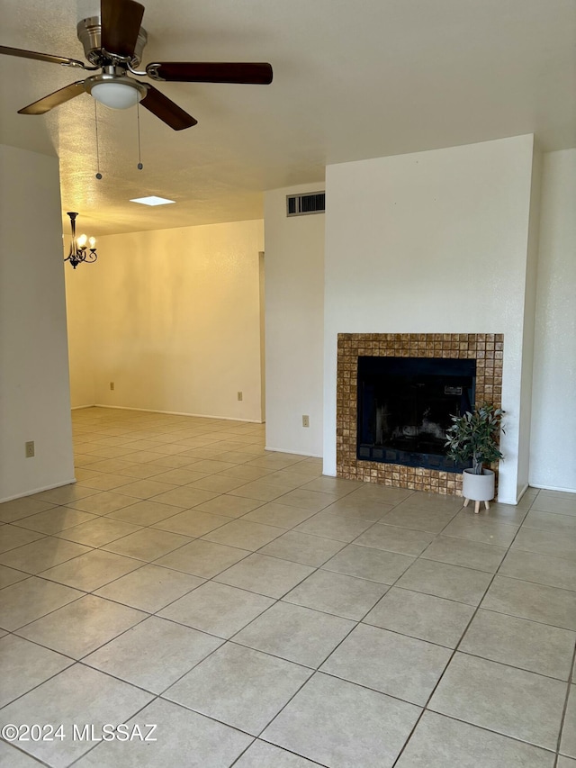 unfurnished living room featuring ceiling fan with notable chandelier, light tile patterned flooring, and a fireplace