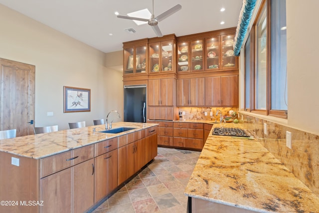 kitchen featuring sink, light stone counters, black refrigerator, an island with sink, and stainless steel gas cooktop