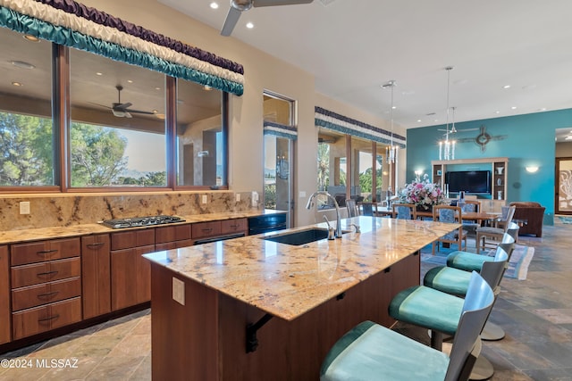 kitchen featuring sink, light stone counters, ceiling fan, an island with sink, and a breakfast bar area