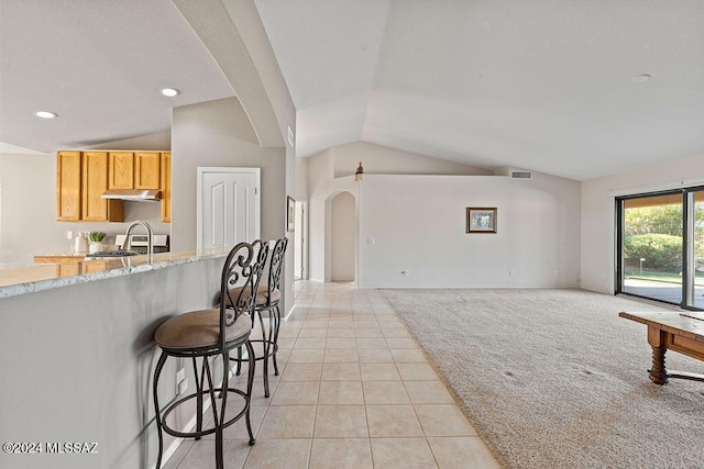 kitchen featuring a kitchen bar, stove, light stone counters, vaulted ceiling, and light tile patterned flooring