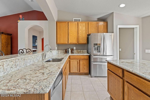 kitchen featuring sink, stainless steel appliances, light stone counters, vaulted ceiling, and light tile patterned flooring