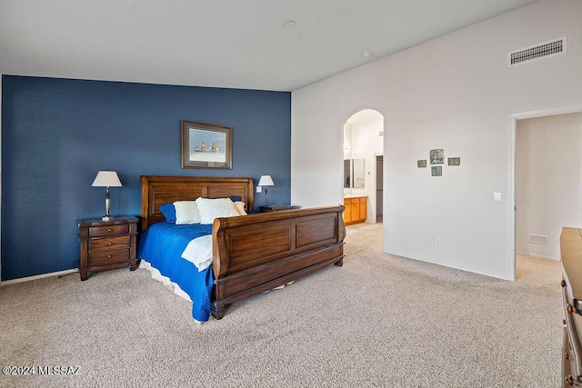 bedroom featuring light carpet, ensuite bathroom, and lofted ceiling