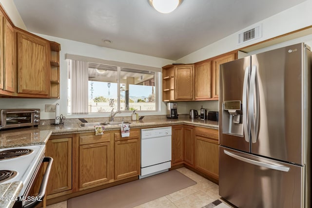 kitchen with light tile patterned flooring, light stone countertops, white appliances, and sink