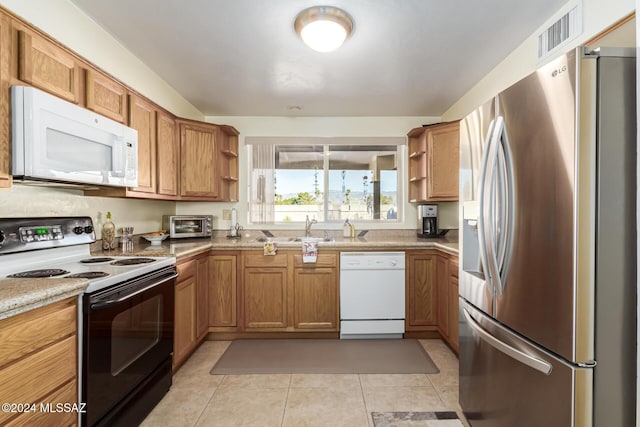 kitchen with light tile patterned flooring, light stone counters, white appliances, and sink