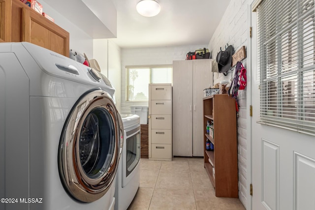 laundry room featuring washer and clothes dryer, cabinets, light tile patterned floors, and brick wall