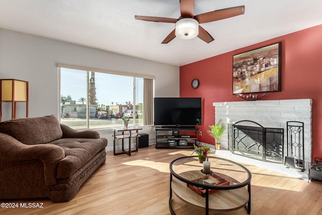 living room featuring ceiling fan, light hardwood / wood-style floors, and a brick fireplace