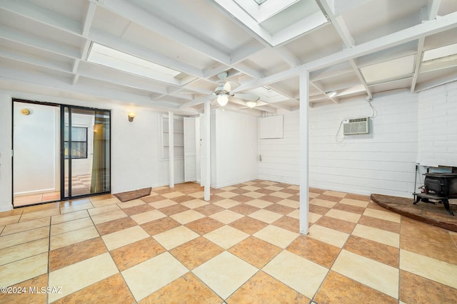 basement featuring wood walls, a wall unit AC, ceiling fan, and a wood stove