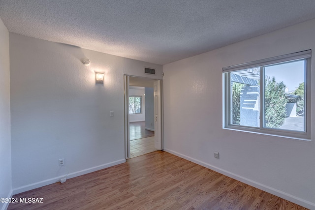 unfurnished room with a textured ceiling, light hardwood / wood-style flooring, and a healthy amount of sunlight