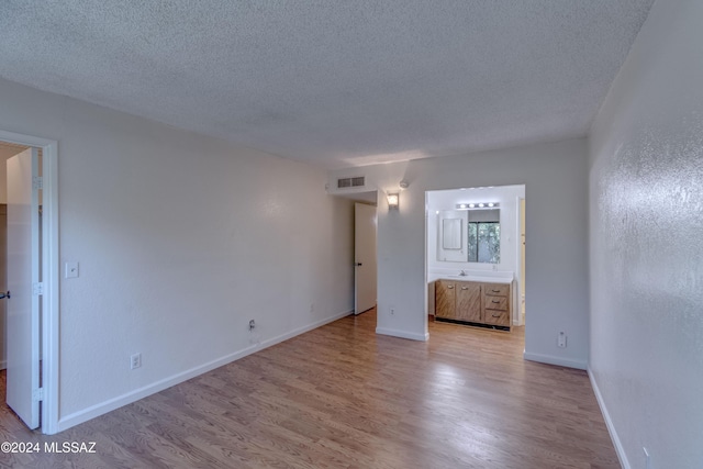 unfurnished bedroom with ensuite bathroom, a textured ceiling, and light wood-type flooring