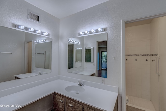 bathroom with vanity, a tile shower, and toilet