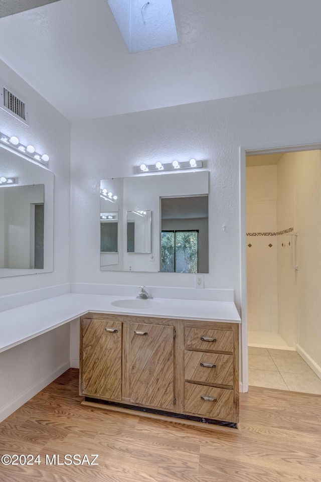 bathroom with hardwood / wood-style floors, vanity, a tile shower, and a skylight