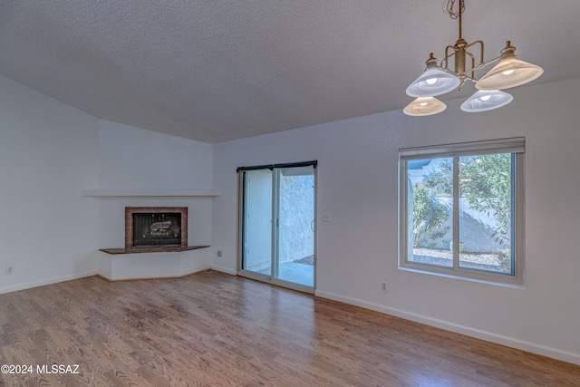 unfurnished living room featuring hardwood / wood-style flooring, a chandelier, and a textured ceiling