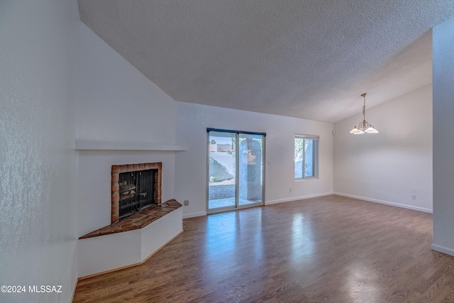 unfurnished living room with vaulted ceiling, hardwood / wood-style floors, a fireplace, a textured ceiling, and an inviting chandelier