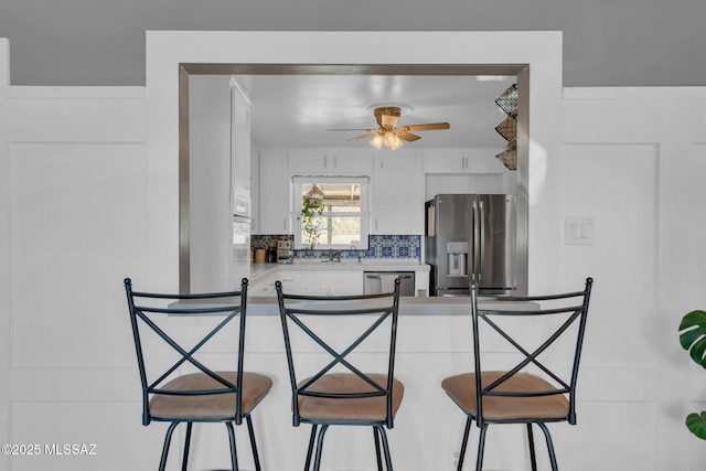 kitchen with tasteful backsplash, stainless steel appliances, ceiling fan, and a kitchen bar