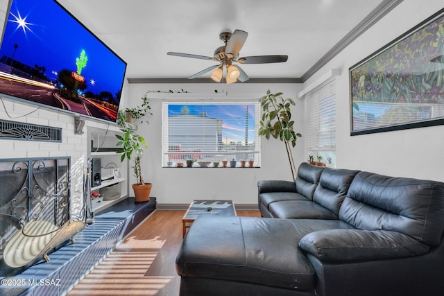 living room with crown molding, ceiling fan, wood-type flooring, and a fireplace