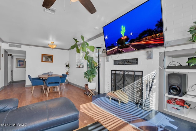 living room featuring hardwood / wood-style flooring, ornamental molding, a brick fireplace, and ceiling fan