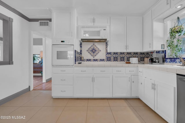 kitchen with tile countertops, white cabinetry, backsplash, light tile patterned floors, and white appliances