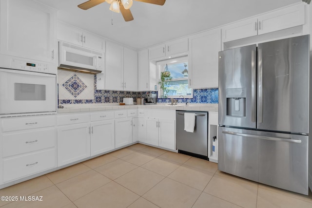 kitchen with light tile patterned flooring, tile counters, white cabinets, stainless steel appliances, and backsplash