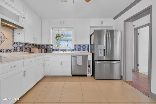 kitchen featuring light tile patterned flooring, white cabinetry, backsplash, tile counters, and stainless steel appliances