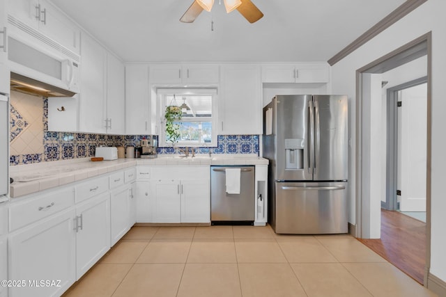 kitchen with appliances with stainless steel finishes, backsplash, white cabinets, light tile patterned flooring, and tile countertops