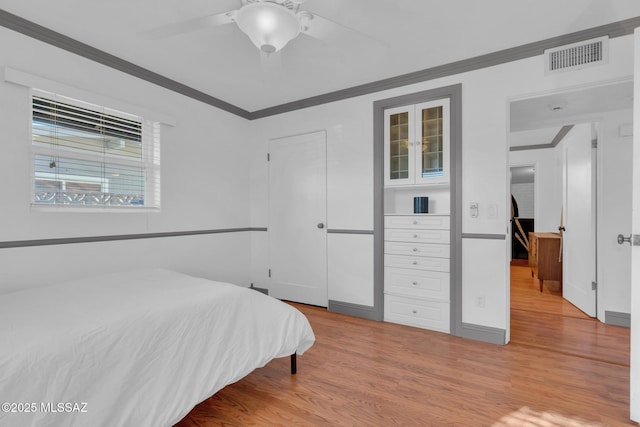 bedroom with light hardwood / wood-style floors, ceiling fan, and ornamental molding