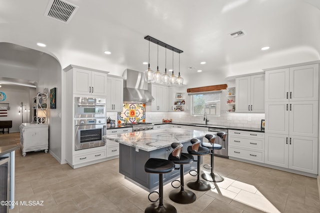 kitchen with decorative backsplash, wall chimney range hood, a center island, white cabinetry, and hanging light fixtures