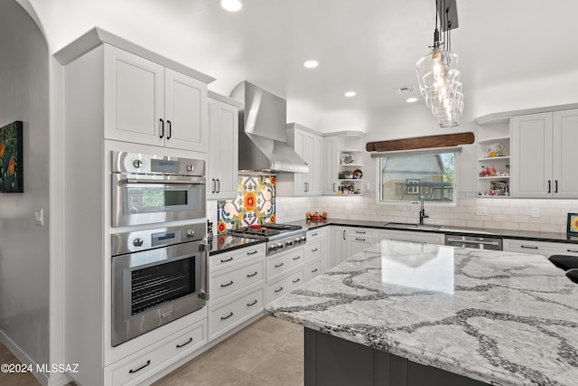 kitchen featuring sink, wall chimney exhaust hood, stainless steel appliances, tasteful backsplash, and decorative light fixtures