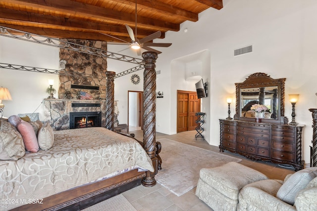 bedroom featuring beamed ceiling, a stone fireplace, wooden ceiling, and a high ceiling