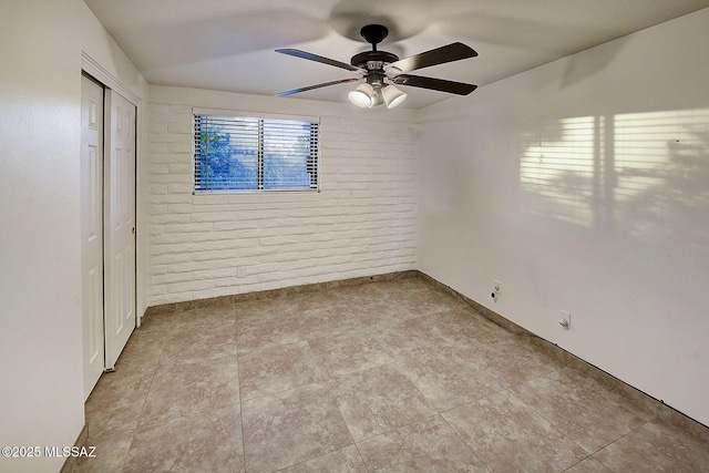 unfurnished room with ceiling fan and brick wall