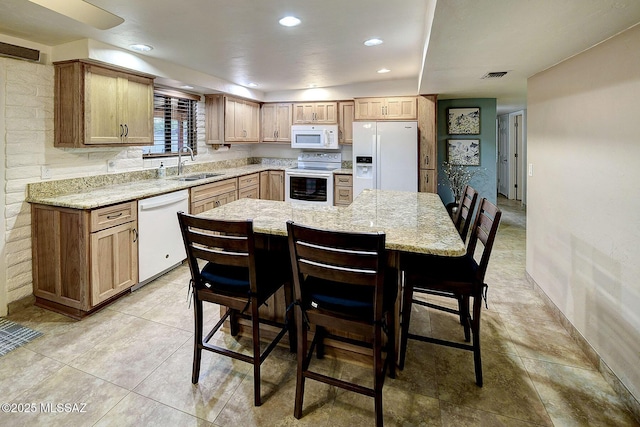 kitchen with light stone countertops, a kitchen breakfast bar, white appliances, and sink