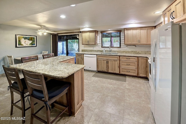 kitchen with white appliances, sink, ceiling fan, light stone countertops, and a kitchen bar