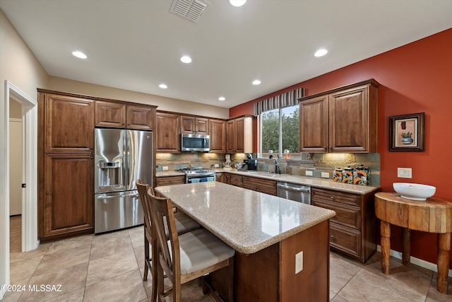 kitchen with a center island, stainless steel appliances, light stone counters, and tasteful backsplash