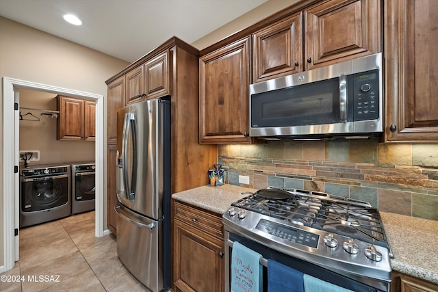 kitchen featuring decorative backsplash, washing machine and dryer, appliances with stainless steel finishes, light tile patterned flooring, and light stone counters