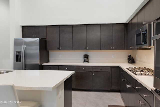 kitchen featuring stainless steel appliances, light tile patterned floors, and dark brown cabinets