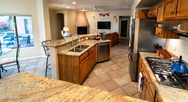 kitchen with a breakfast bar, ventilation hood, sink, ceiling fan, and stainless steel appliances