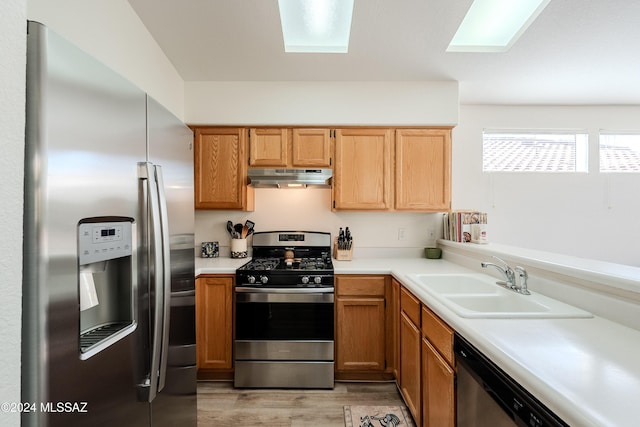 kitchen featuring a skylight, sink, stainless steel appliances, and light hardwood / wood-style flooring