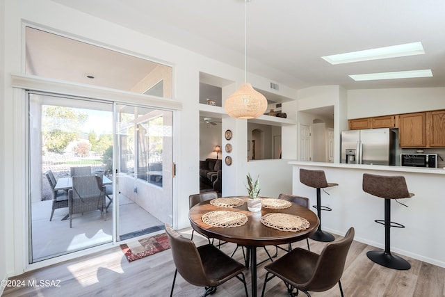 dining space featuring light hardwood / wood-style flooring and vaulted ceiling with skylight